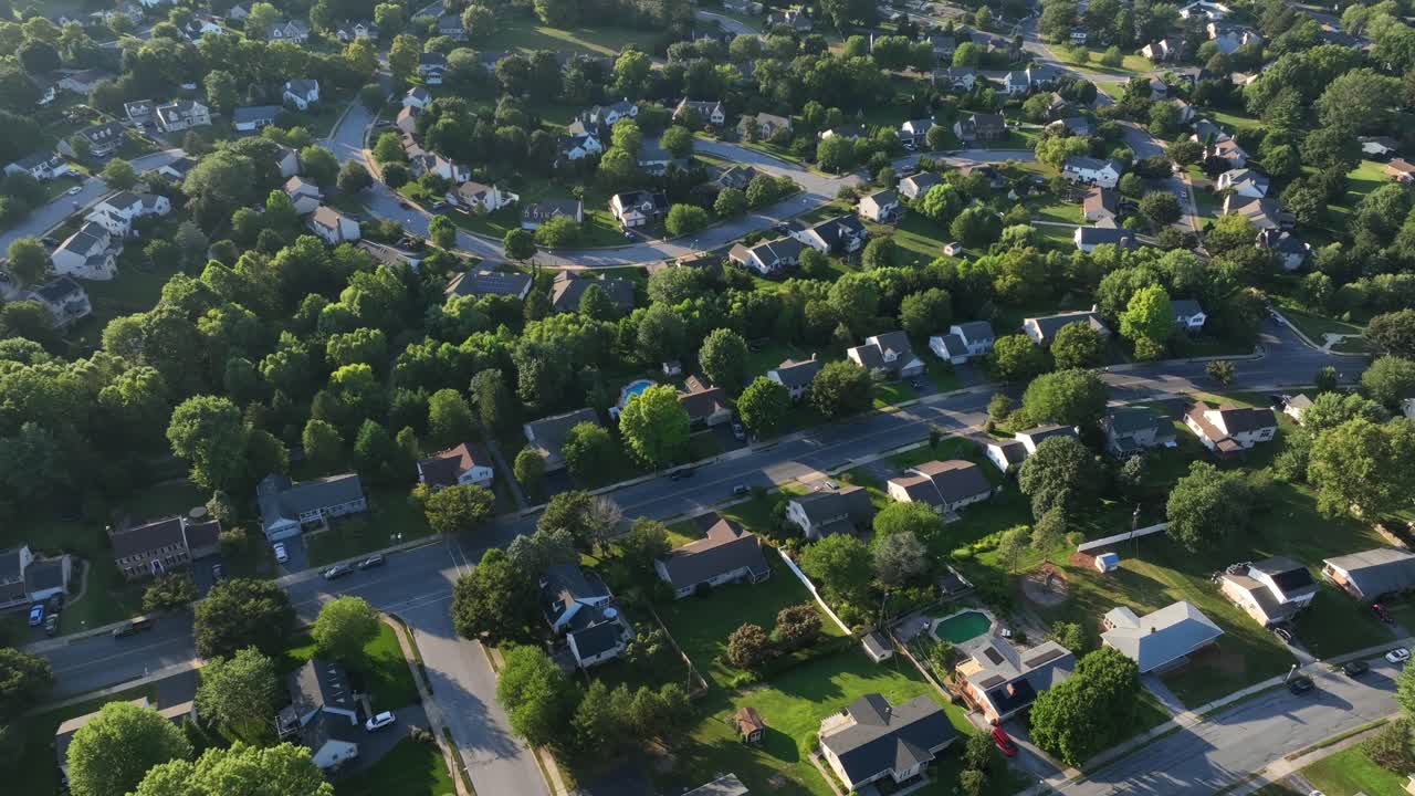 Upper class residential area in suburbia of town in summer. Green blooming trees in upscale neighborhood of America. Driving car on street. Sunset time. Aerial top down. Pool in garden