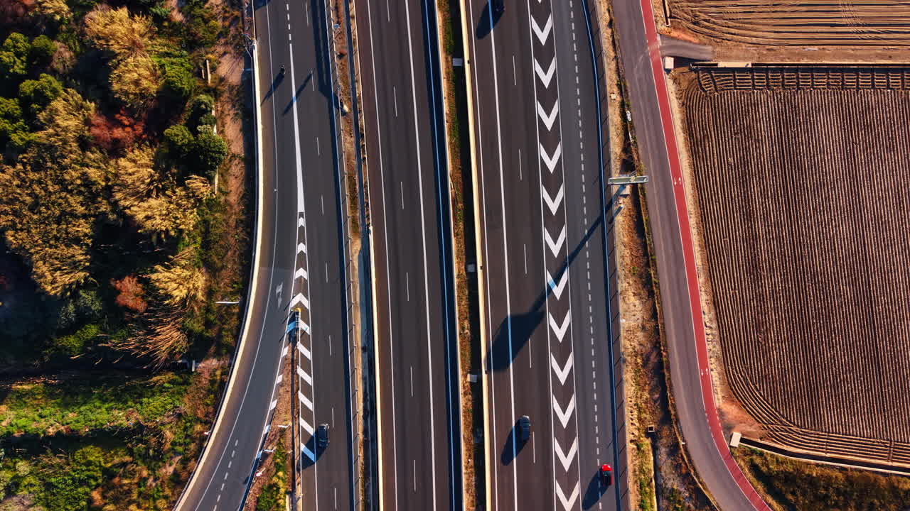 高速道路の車線とシェブロン標識の上空からの空撮。白いシェブロン路面標示、歩道橋、そして近くにある赤い舗装された自転車レーンがある高速道路の交通の俯瞰図。