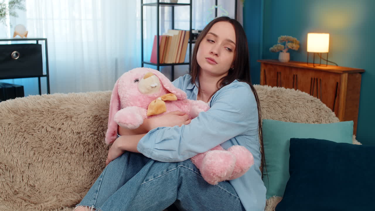Woman on sofa hugging plush bunny feeling lonely romantic missing beloved tenderness divorce