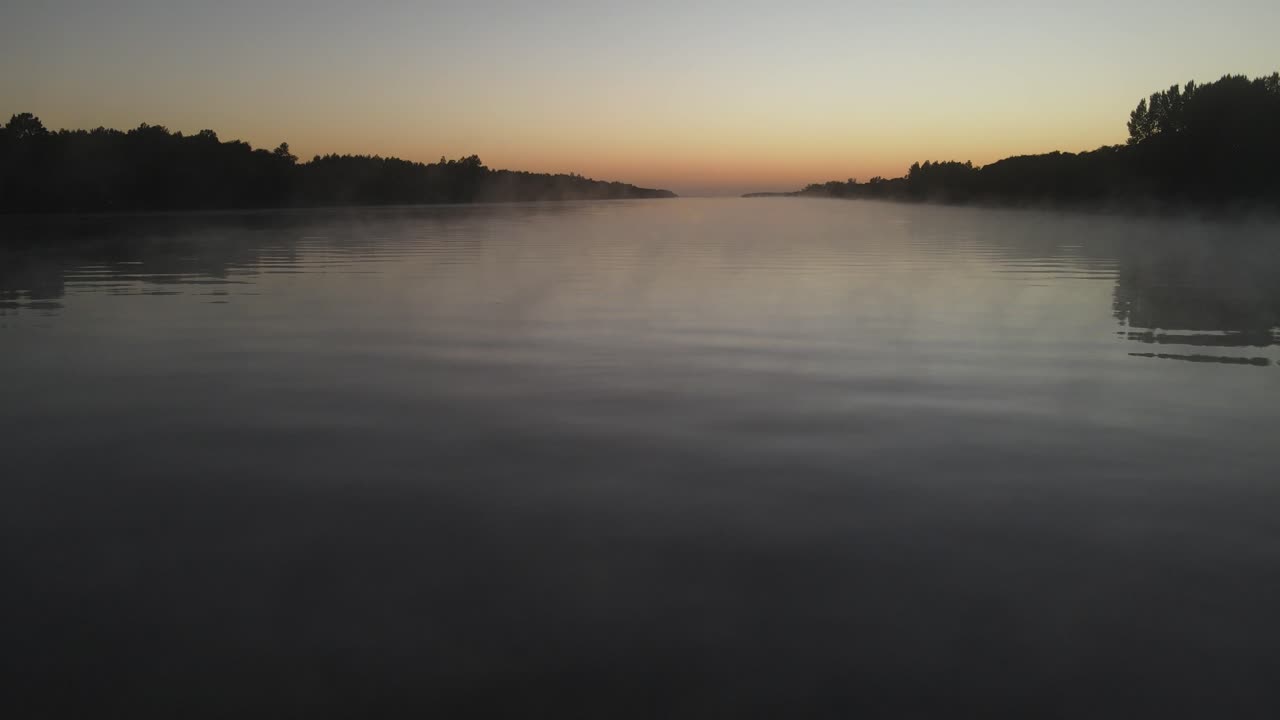 Mystical low angle drone flight over foggy tranquil amazon river during colorful sunrise in background. Silhouette of trees on shore. Aerial view 4K