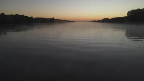 mystical low angle drone flight over foggy tranquil amazon river during colorful sunrise in background. silhouette of trees on shore. aerial view 4k