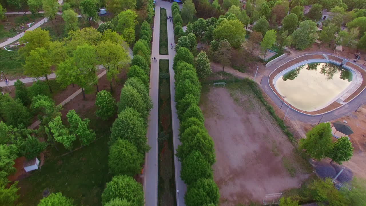 Green town park zone with artificial pond. Walking roads leading to the big shopping mall. Aerial view.