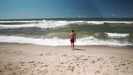 joven en shorts rojos va al mar en una playa