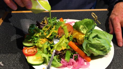 Male-hand-is-seen-pouring-green-dressing-over-fresh-salad-with-lettuce,-onions-and-tomatoes-for-a-healthy-appetizer-meal