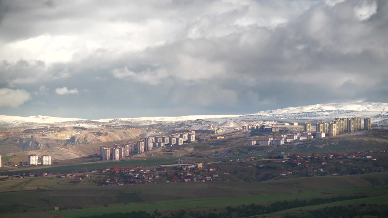 Vista panoramica di edifici residenziali e montagne innevate sotto un cielo nuvoloso