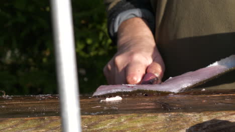 Close-up-of-male-hands-cutting-fish-fillet-on-wooden-board-outdoors