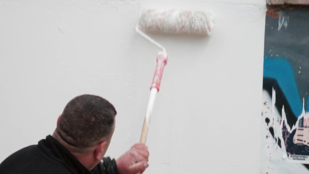 Primo piano di un uomo che dipinge un muro usando un rullo, coprendo dei graffiti