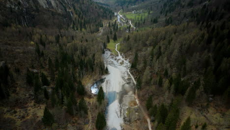 aerial pullback of idyllic hiking trail in valley of val di mello natural reserve with pine trees and crystal clear river during summer