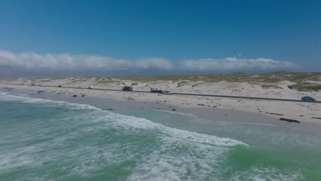 Autos-Fahren-Viel-Befahrene-Straße.-Ziehen-Sie-Aufnahmen-Von-Personen-Zurück,-Die-Am-Sandstrand-In-Richtung-Rollender-Wellen-Gehen.