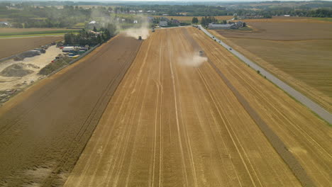 Camino-Largo-Y-Sinuoso-Entre-Amplias-Tierras-De-Cultivo-En-Kielno,-Polonia-Con-Tractores-Cosechando-Cultivos-En-Un-Día-Soleado---Drone-Aéreo---Toma-De-Retroceso