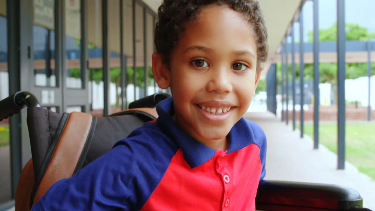 Front view of happy disabled African American schoolboy sitting on wheelchair in school corridor 4k