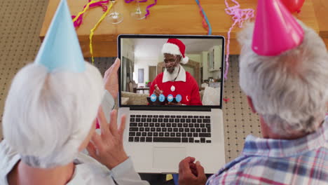 pareja de adultos mayores caucásicos con sombreros de fiesta en la computadora portátil video chat durante la navidad en casa