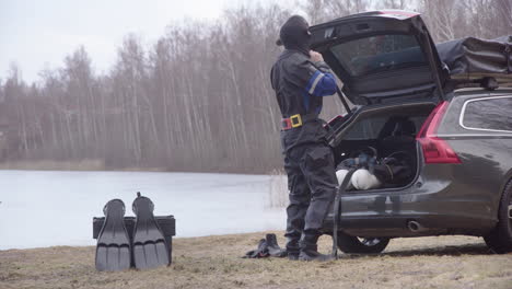 Scuba-diver-in-dry-suit-gears-up-from-car-trunk-for-penetration-dive-in-icy-lake