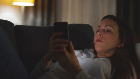 close up of woman lying on sofa at home at streaming or watching movie or show or scrolling internet on mobile phone 11