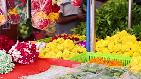 a vendor wearing gloves arranges vibrant yellow marigold garlands at a colorful outdoor flower market in singapore, under bright natural daylight with a steady camera view