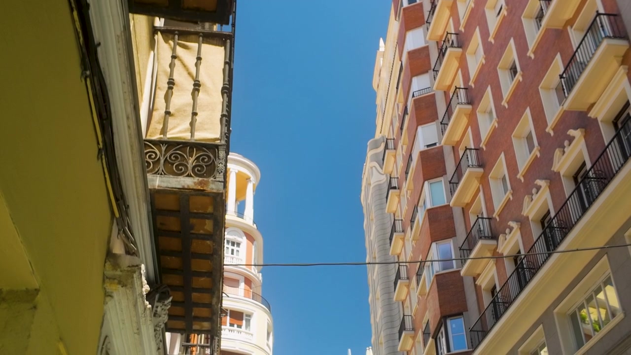 Uma vista de baixo ângulo da arquitetura residencial histórica e moderna em Madri, Espanha, exibindo varandas e fachadas vibrantes contra um céu azul claro.