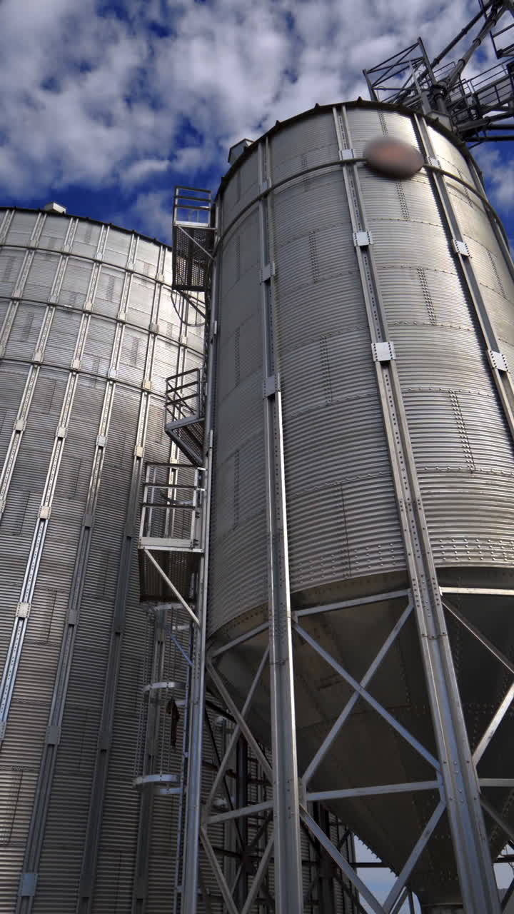 Modern granary outdoors. Metallic elevators for storing grain. Agricultural complex with big aluminum containers under the blue sky. Vertical video