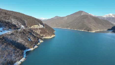 A snowy mountain lake, surrounded by tree-dotted hills and glistening in the sunlight, offers a captivating view of winter's untouched beauty