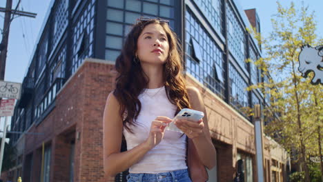 una mujer joven usa un teléfono inteligente de pie en una encrucijada. una chica asiática mirando el teléfono.