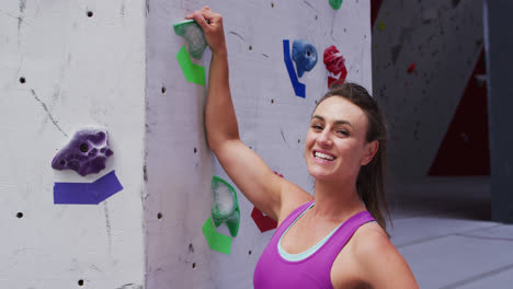retrato de una mujer caucásica sonriente agarrando una empuñadura en una pared de escalada en una parede de escalada interior
