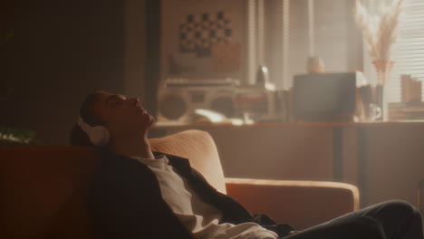 young man in headphones leaning back on sofa, enjoying music with eyes closed