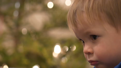 tired toddler with empty eyes in front of christmas tree, close up