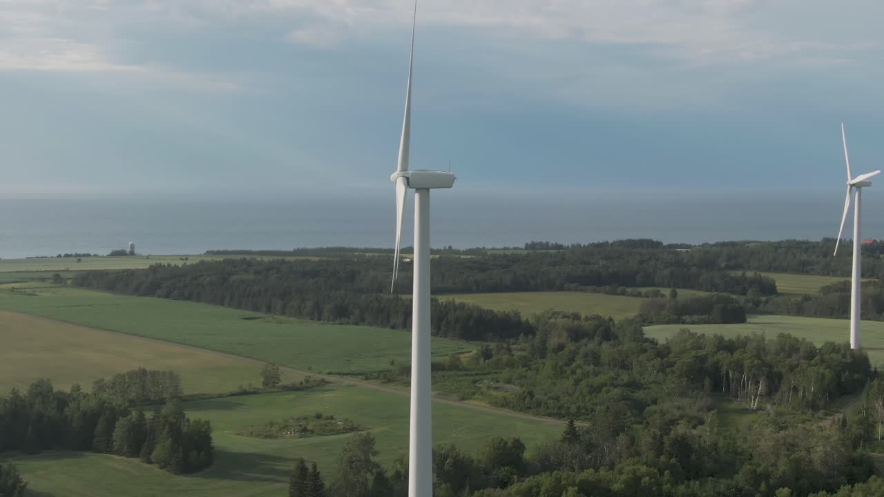 Turbine eoliche che sfruttano l'energia del vento convertendo elettricità in mezzo a un campo verde sotto il cielo blu estivo a St. Laurent, Quebec settentrionale, Canada. Panoramica ravvicinata.