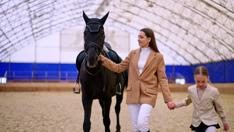 mother and daughter with a horse in an indoor arena