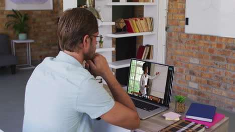 hombre de negocios caucásico sentado en un escritorio usando una computadora portátil haciendo una videollamada con una colega