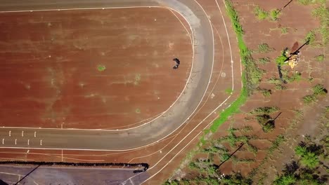 a drone, top down, aerial, panning view of a go cart race track with tropical vegetation, brown soil, and dirt