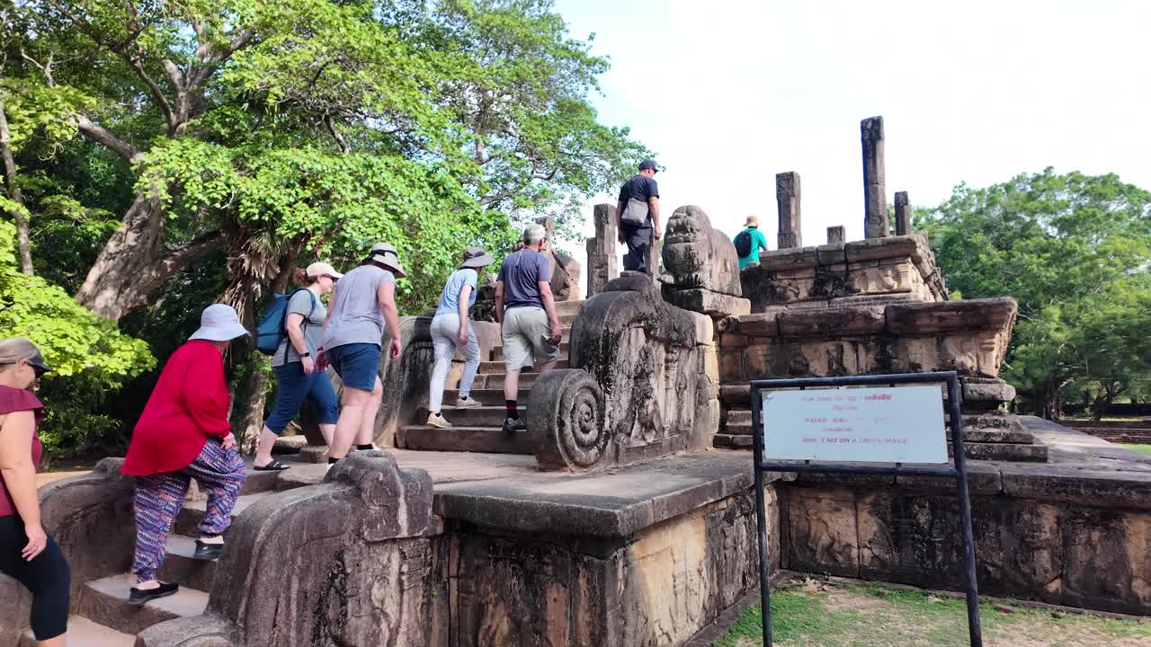 Tourists exploring the ancient ruins of the council chamber in Polonnaruwa, Sri Lanka, surrounded by lush greenery and historical architecture.