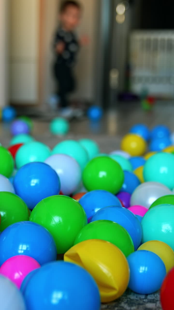 Little baby comes into the room. Toddler boy stops surprised by the multiple balls in the middle of the room. Blurred backdrop. Vertical video