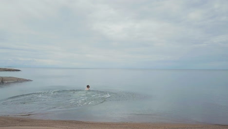 tracking aerial man runs on beautiful ocean beach and dives into calm water