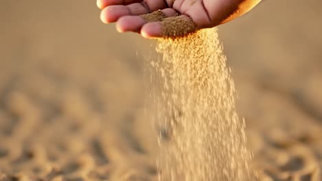 a hand with sand falling through the fingers at sunset