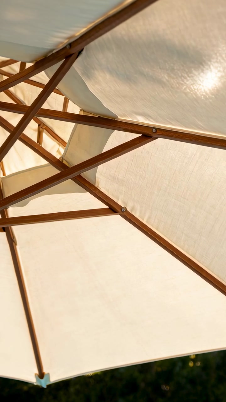 Vertical video: Tilting camera revealing patio umbrella in yard with cream canopy ribs and bolts
