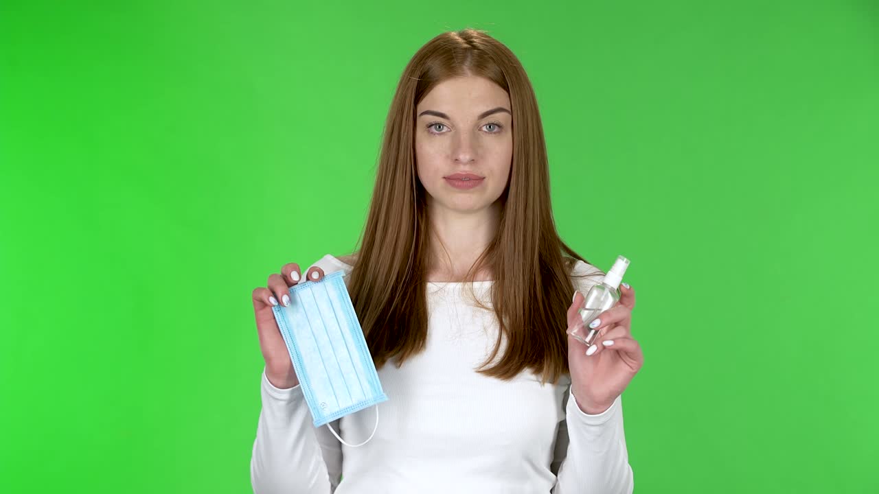 Portrait of pretty young girl is looking straight and holding in hands a medical mask and an antiseptic