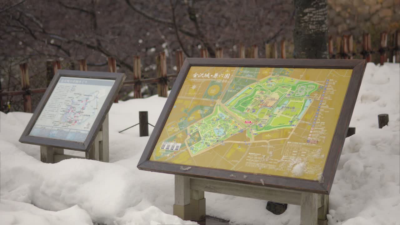 A detailed map of Kanazawa Castle and Kenrokuen Garden in Japan, covered in snow on a winter day. The scene captures the serene beauty of the historic site during snowfall. Static shot