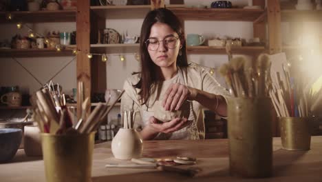 young woman potter forming a bowl out of soft clay with her hands in the art studio