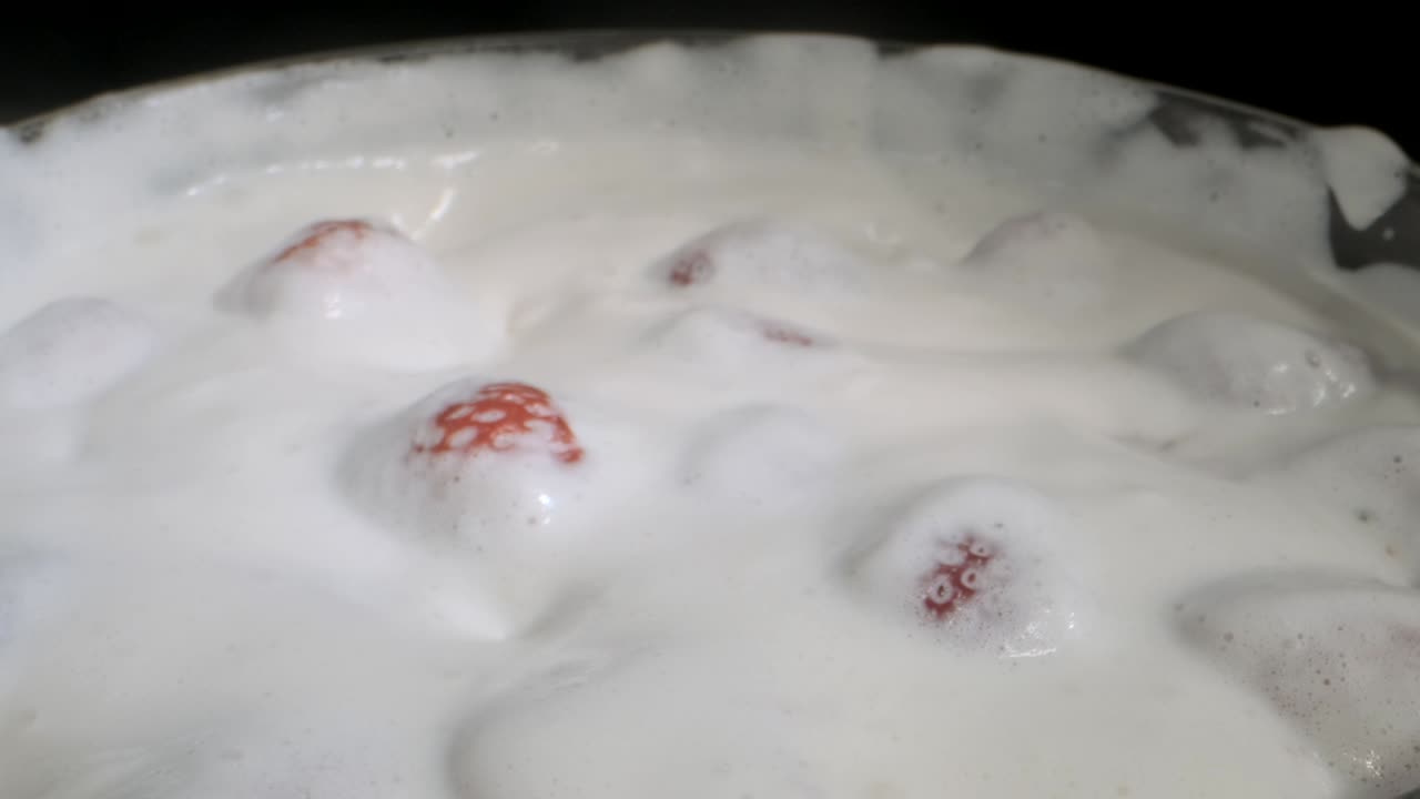 girar fresas maduras cubiertas con una capa gruesa de crema en vidrio sobre fondo negro. rotación de la cámara 360 grados, primer plano.