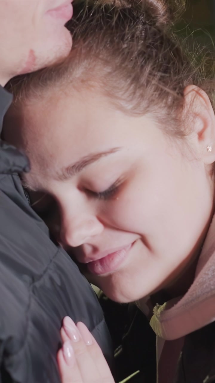 Il profilo dell'uomo rimane costante per tutta la sequenza. La donna posiziona la mano vicino alla parte inferiore della testa e del collo. Luci verdi sfocate suggeriscono un'illuminazione artificiale di notte.