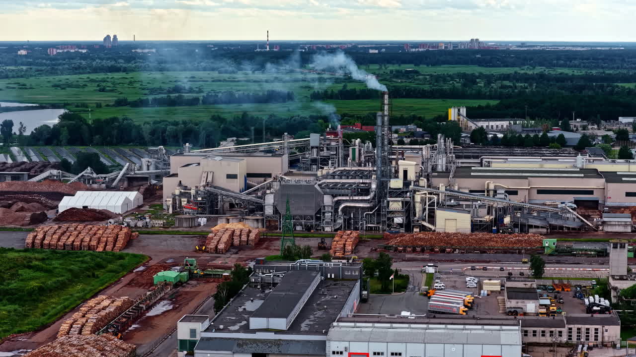 Aerial shot captures the massive Bolderaja Ltd industrial complex, a timber processing and particleboard manufacturing plant in Riga, with smoke rising from its smokestacks over vast lumber yards
