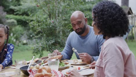 Happy-biracial-parents-and-daughter-eating-meal-at-dinner-table-in-garden,-slow-motion