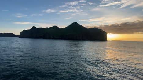 Tiny-island-with-town-in-Southern-part-of-Iceland-during-sunset,-view-from-sailing-vessel