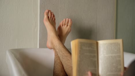 man reading book while lying in bathtub at home 4k