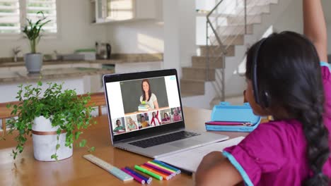 Schoolgirl-using-laptop-for-online-lesson-at-home,-with-diverse-teacher-and-class-on-screen