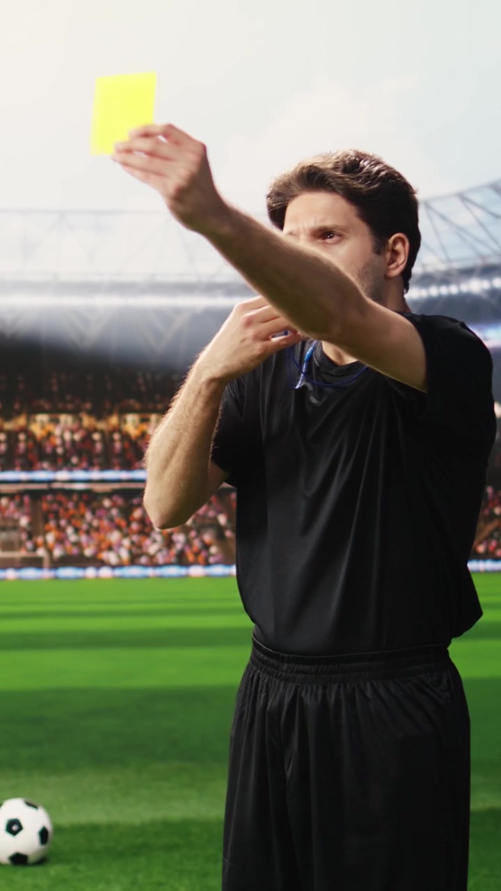 Video verticale: Arbitro di calcio in nero che mostra un cartellino giallo a un giocatore che protesta sul campo.