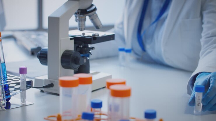Close Up Of Lab Worker Conducting Research Using Microscope Holding Test Tube Labelled Delta