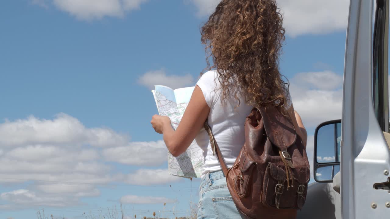 mujer alegre leyendo un mapa de papel cerca del coche