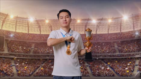 금메달과 트로피를 들고 있는 아시아인 남자가 가을 만지고 웃으며 카메라를 가리키며 경기장에서 자부심을 느다.