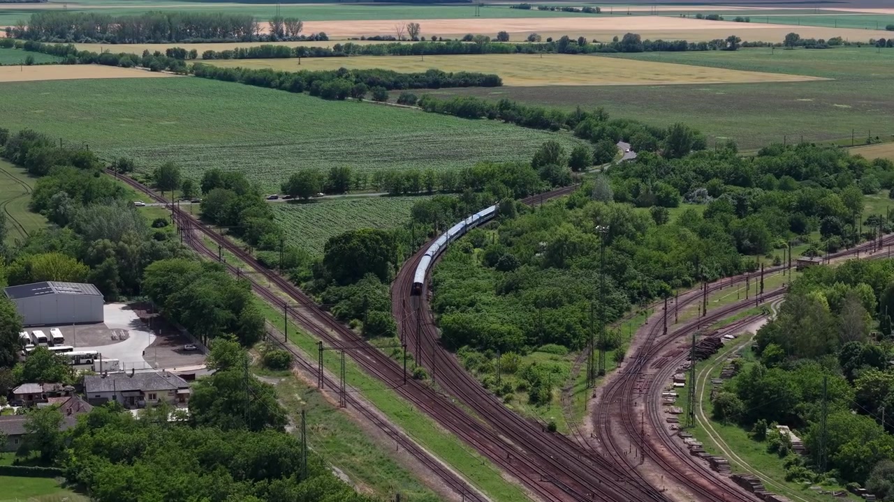 Letecký záběr dronem osobního vlaku projíždějícího železniční křižovatkou uprostřed venkovských polí Maďarska v létě.